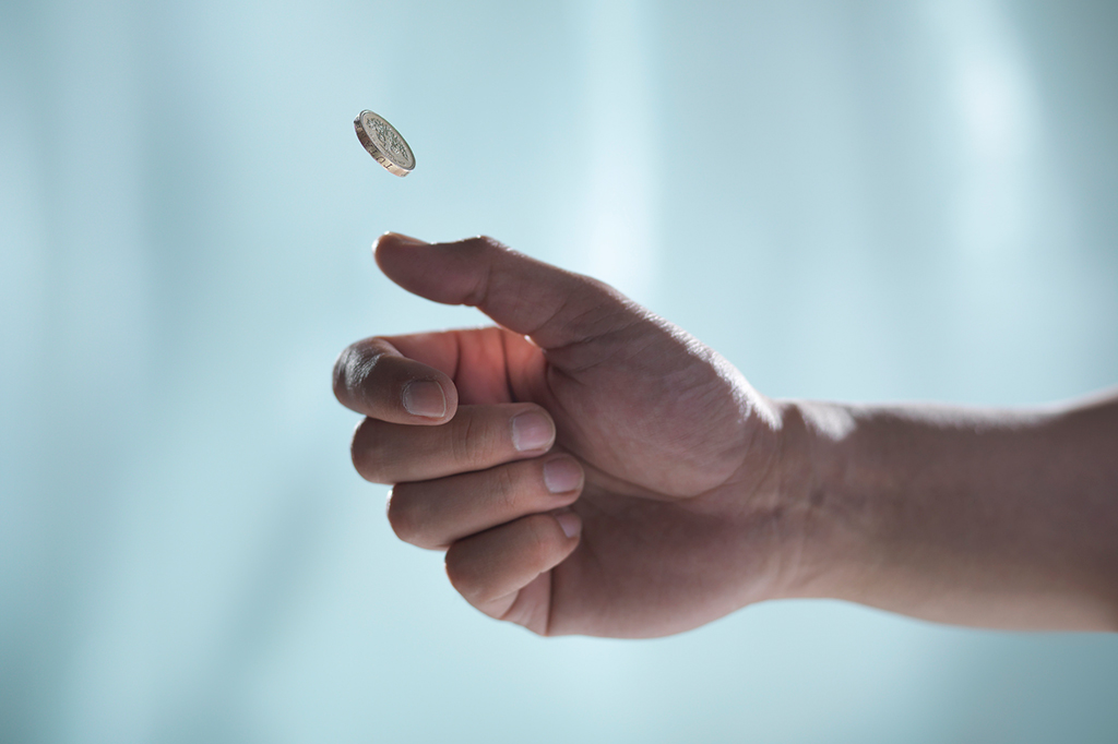 Foto aproximada de uma mão masculina jogando uma moeda para cima.