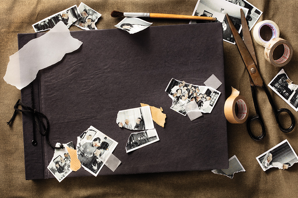 Foto de um álbum de família visto de cima, com alguns pedaços de fotos, papéis recortados e materiais como tesouras e fitas adesivas em cima e ao redor dele.
