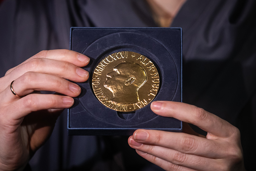 Zoom das mãos de uma pessoa segurando uma medalha do Prêmio Nobel.