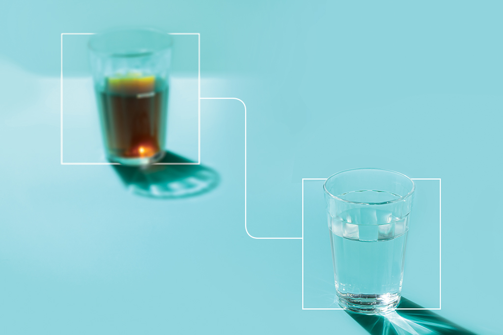 Foto de dois copos americanos, o da esquerda está desfocado e preenchido com café dentro, enquanto o da direita está focado e com água dentro.