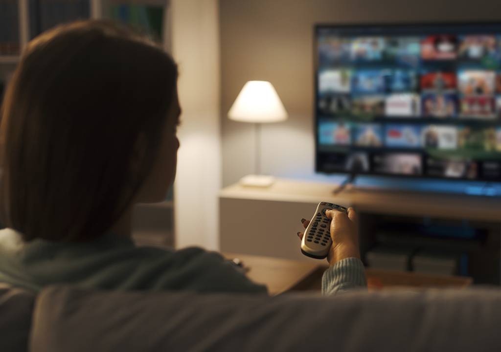 Mulher jovem segurando um controle e apontando-o para a televisão.