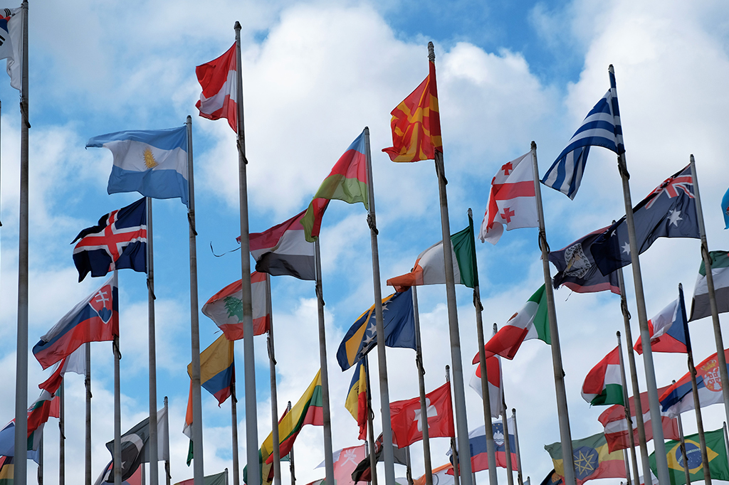 Bandeiras de diferentes países tremulando em céu aberto.