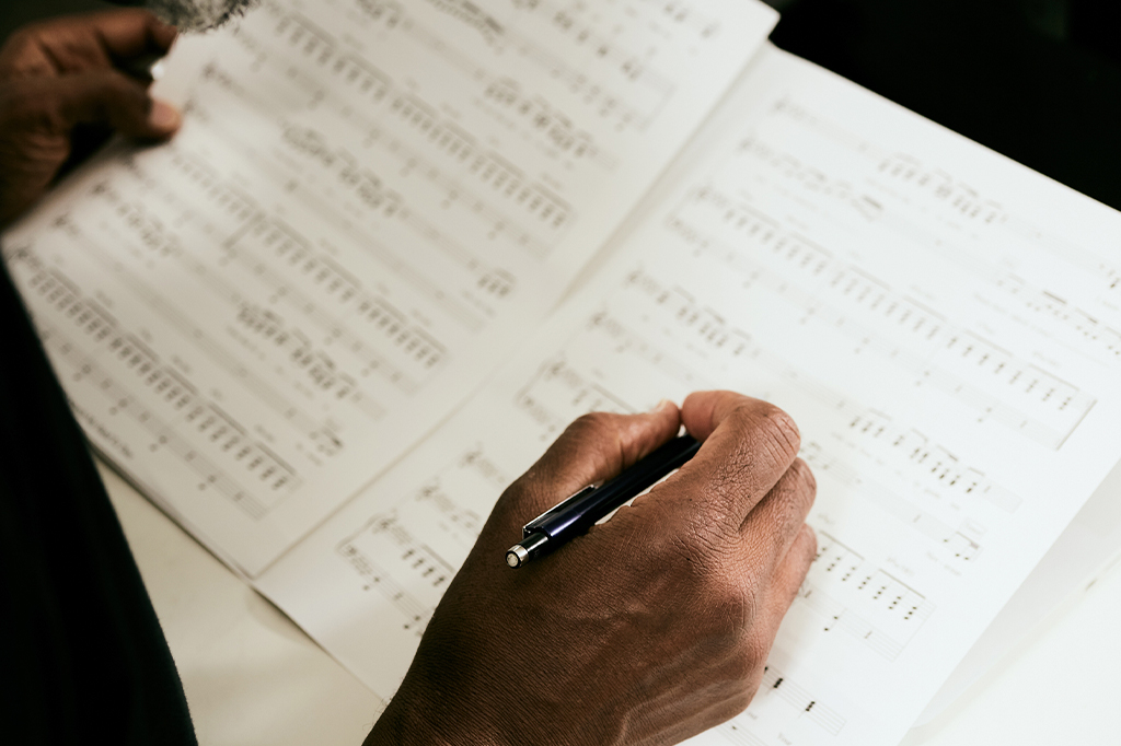 Foto aproximada das mãos de um negro escrevendo pauta musical.