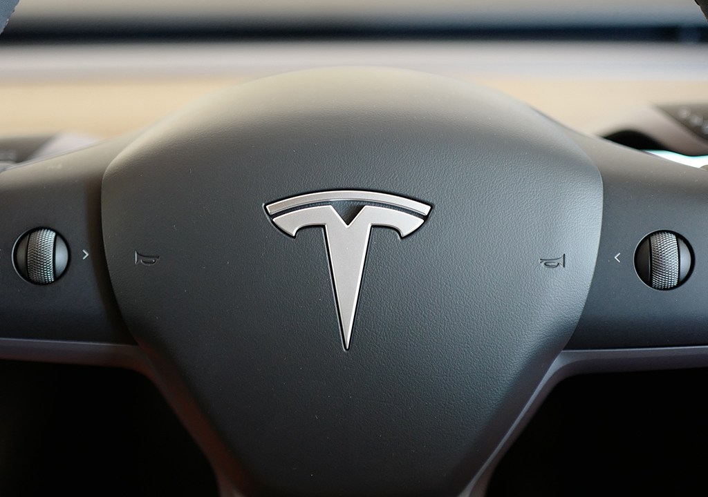Volante de um carro com o Logo da marca Tesla em destaque.