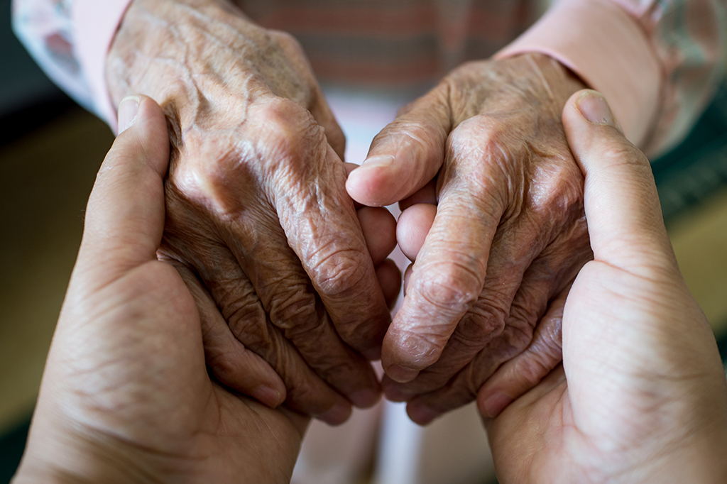Mão de uma pessoa jovem segurando a mão de um idoso.