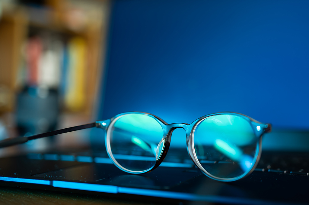 Um óculos com lentes com filtro de tela azul em cima de um notebook.