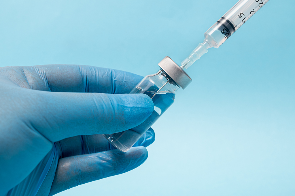 Mão com luva segurando uma seringa de vacina.