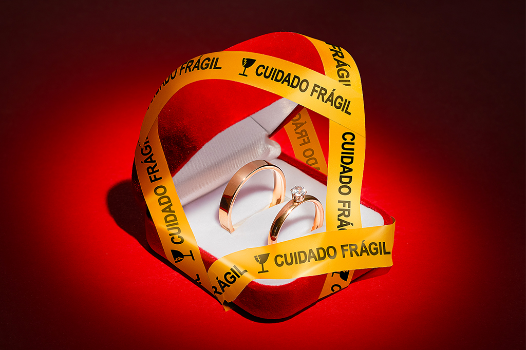 Foto de uma caixa com duas alianças e diversas fitas escrito “Cuidado frágil” envolta dela.