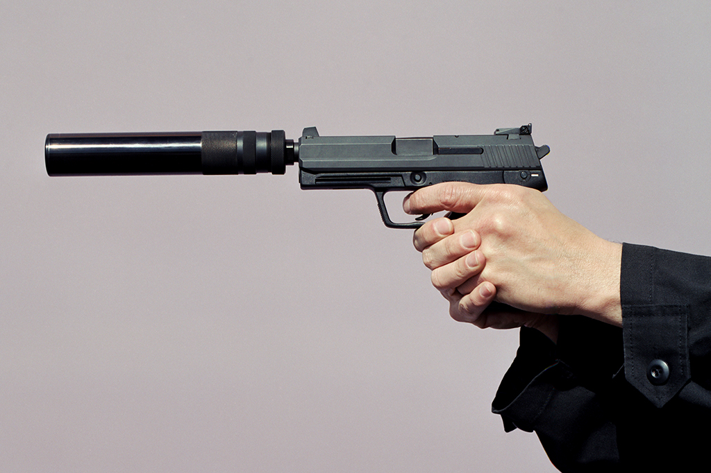 Foto de uma mão segurando uma arma com silenciador.