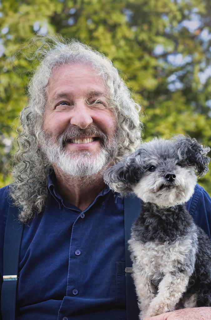 Um homem de cabelo cacheados e brancos ao lado de seu cachorro.