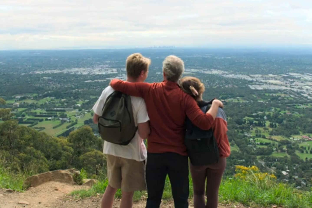 Três jovens em uma montanha de uma cidade. Eles estão abraçados.