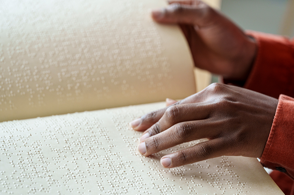 Zoom nas mãos de uma pessoa lendo braille.