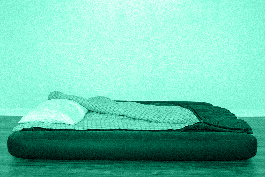 Colchão de ar com travesseiro e lençol, em ambiente vazio.
