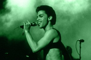 Retrato de Prince em show, segurando microfone enquanto canta.