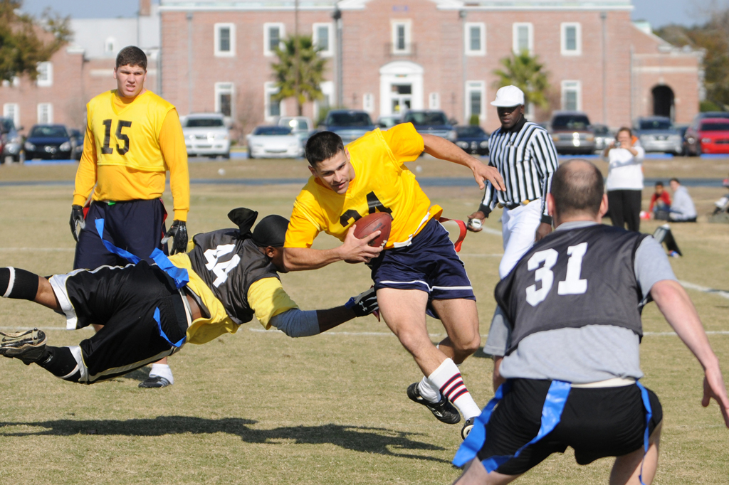 Homens em uma campo com gramado praticando flag football.