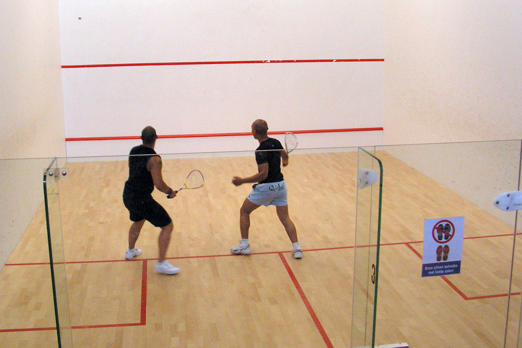 Dupla de homens praticando squash em uma sala.