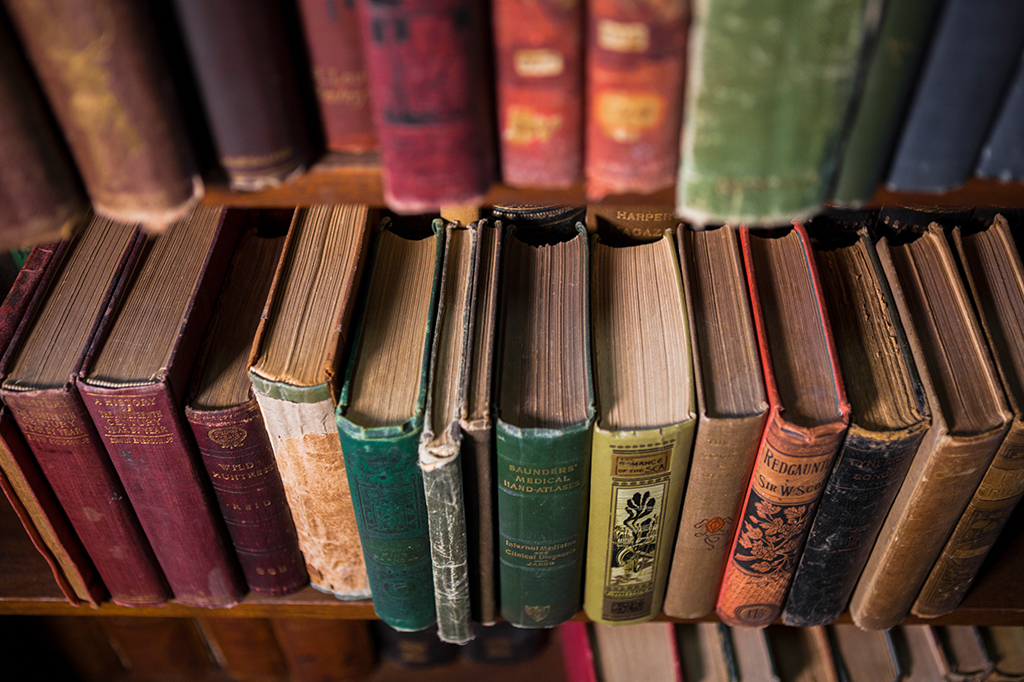 Livros antigos empilhados em uma prateleira.