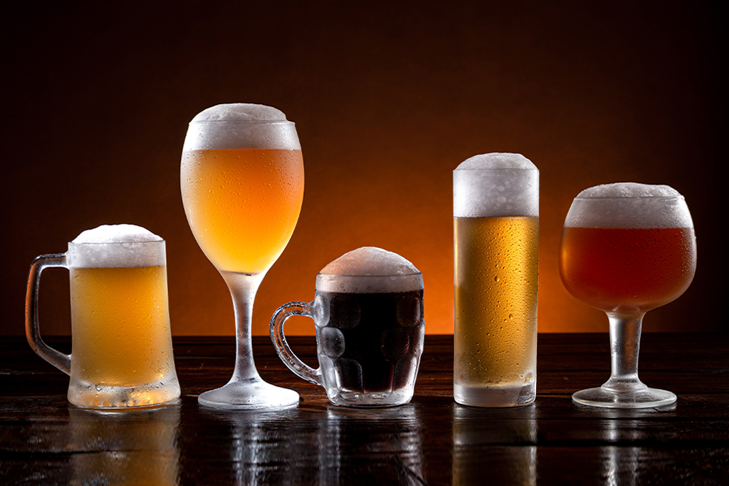Foto de Variedade de cervejas em copos diferentes na base de madeira. Fundo escuro e laranja.