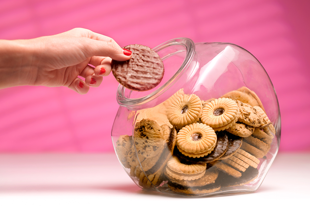 Fotografia de uma mão feminina roubando biscoito do pote de biscoitos.