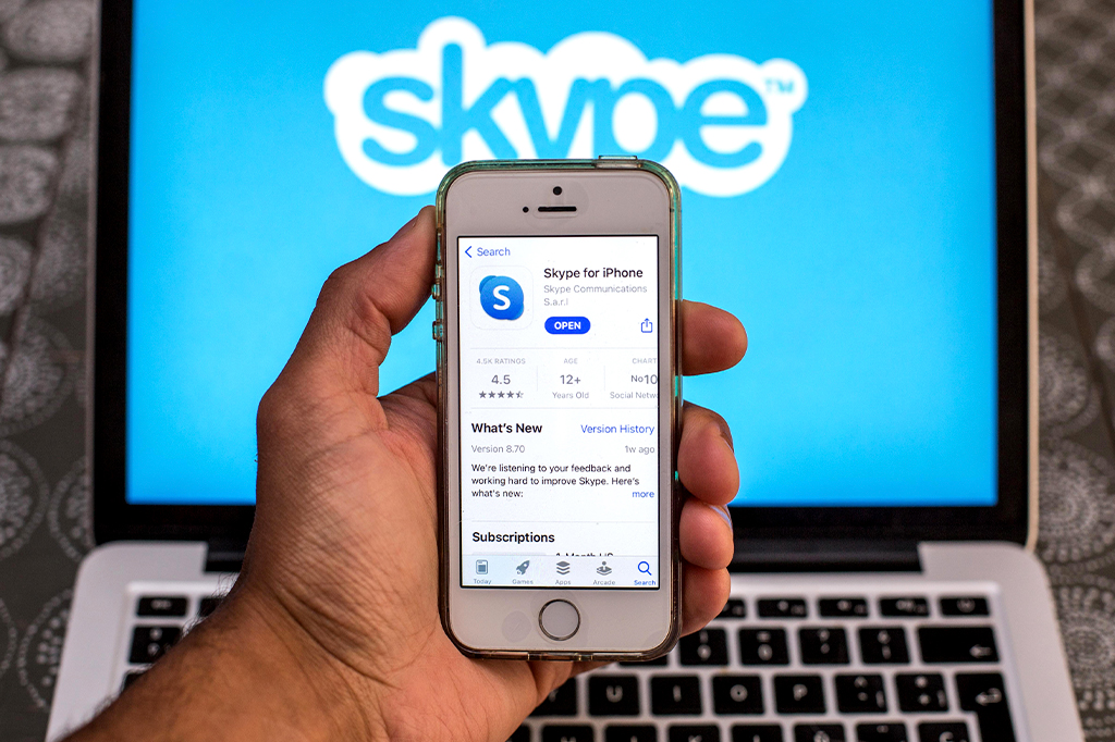 Fotografia do aplicativo do Skype na App Store é exibido na tela de um smartphone, com o logotipo do Skype exibido em um laptop ao fundo.