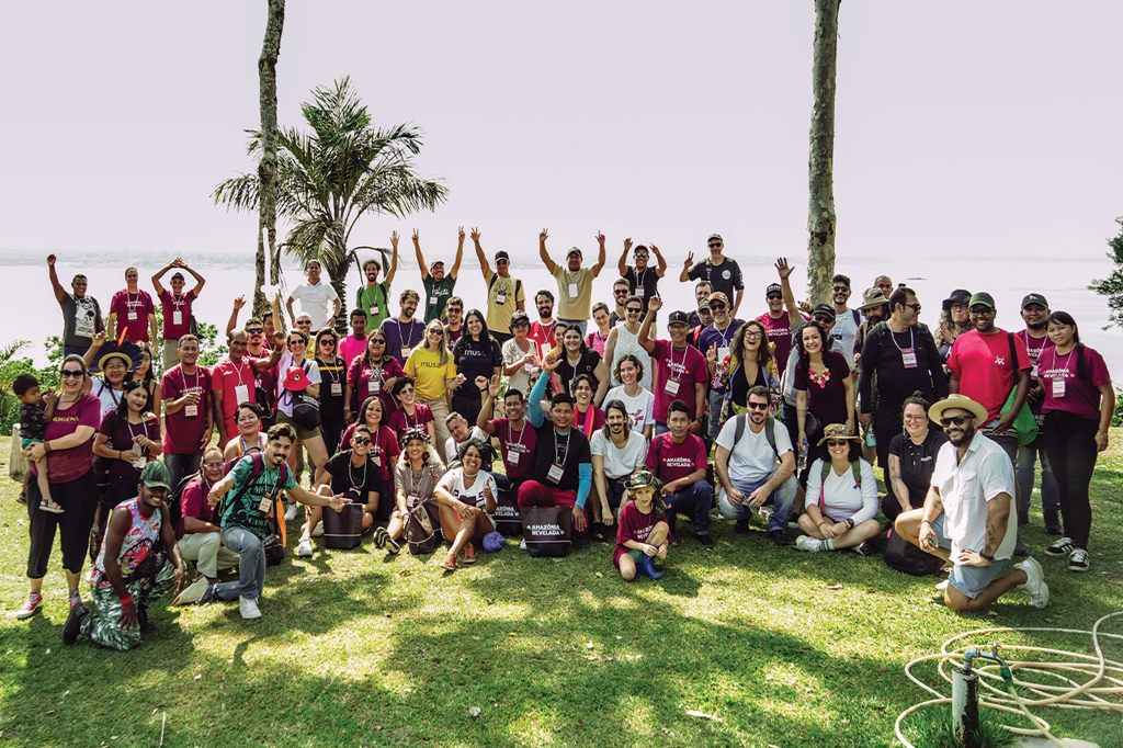 Imagem de um grupo de pessoas reunidas, num gramado, na beira de um rio.