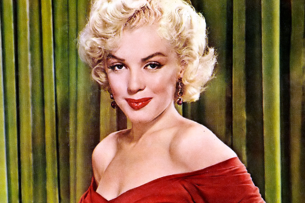 Imagem de uma mulher sorrindo, com cabelos curtos e loiros, vestindo um vestido vermelho.