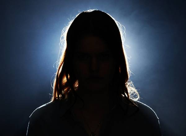 Fotografia de uma mulher no escuro com uma luz forte branca atrás dela.