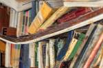 Imagem de uma prateleira curvada com livros velhos e úmidos em uma biblioteca abandonada.