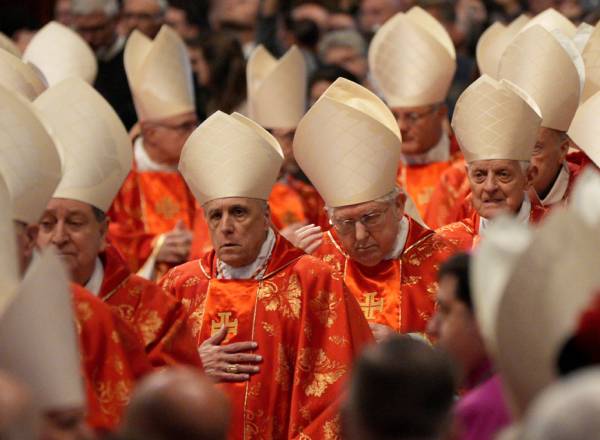 Imagem de dezenas de Cardeais, com a tradicional roupa vermelha e chapéu branco, reunidos numa missa no Vaticano.