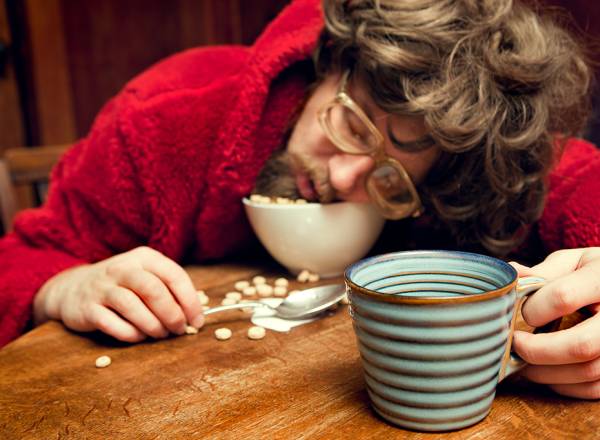Fotografia de um homem dormindo em cereais com café na mão.
