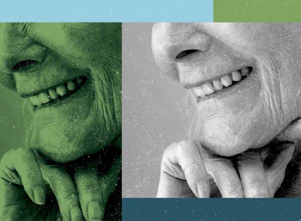 Imagem, close up, de uma mulher idosa sorrindo com a mão no queixo.