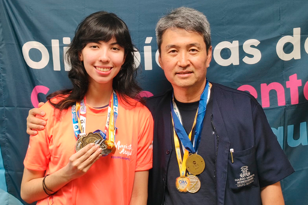 Fotografia de Marcela Sayumi e seu pai e professor, Sandro Yoshio Kuriyama segurando as medalhas.