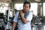 Fotografia de um homem idoso asiático com dor no ombro durante exercícios na academia.