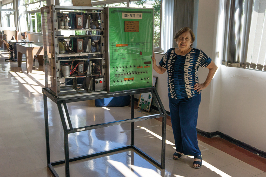 Imagem de uma mulher idosa ao lado do antigo computador LSD &ndash; Pato Feio.