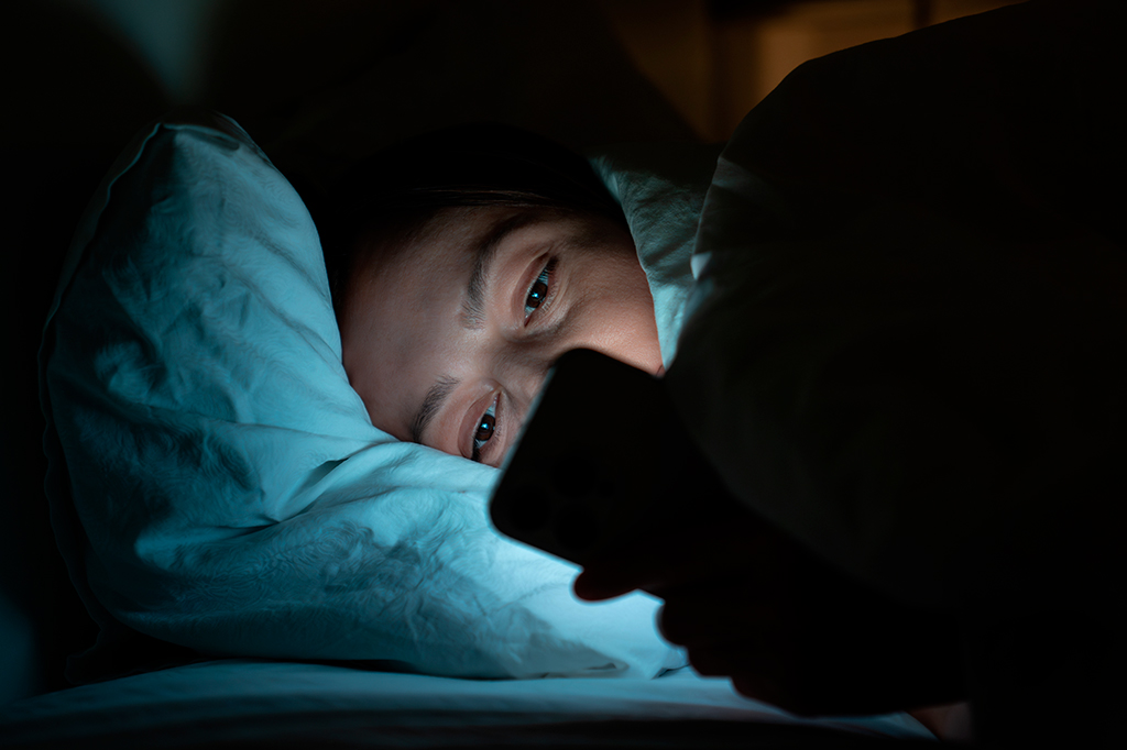 Fotografia de uma mulher deitada vidrada no celular.