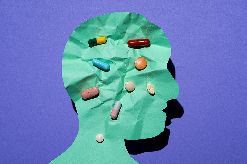 Fotografia de uma silhueta humana recortada em papel, o papel está amassado com remédios sobre o papel.