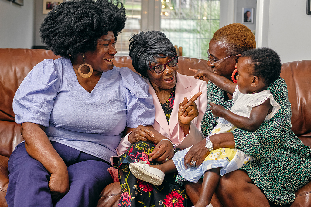 Fotografia de mulheres negras de idades diferentes sentadas no sofá com mãe idosa e bebê.