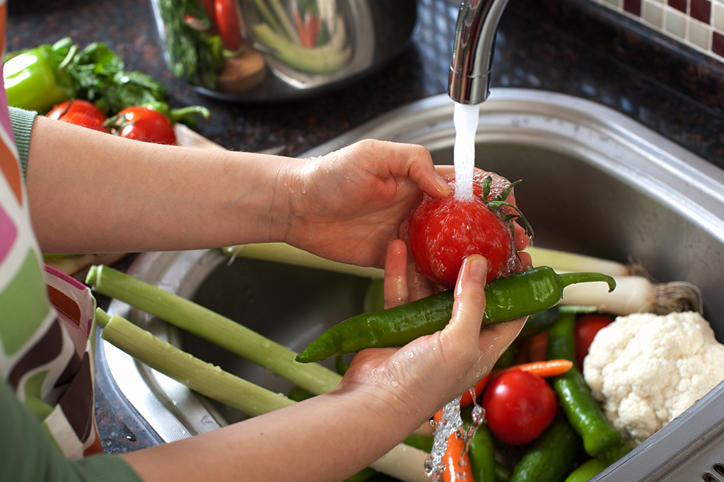 Fotografia de uma mulher lavando legumes na cozinha.