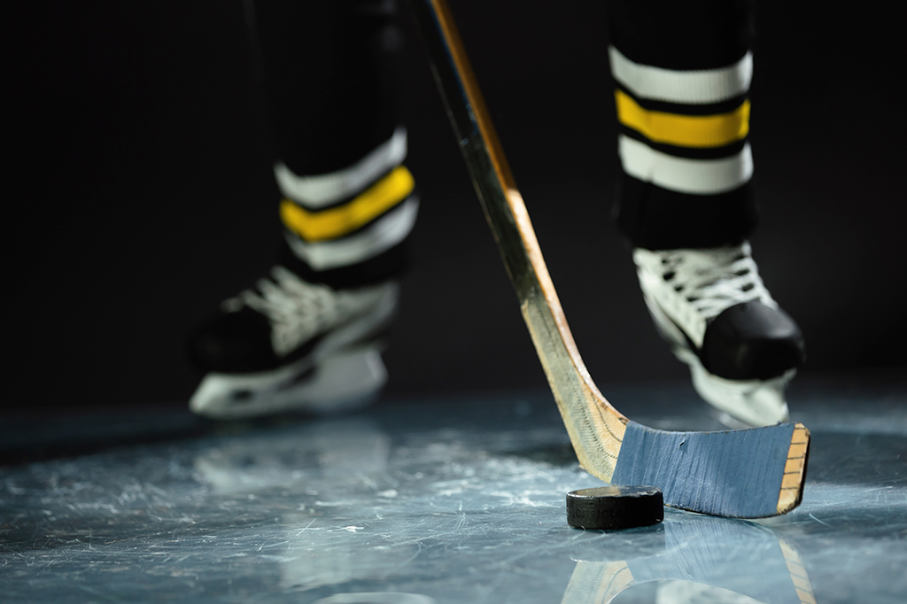 Fotografia de um jogador de hóquei dee patins em pé com um taco hóquei e um disco.