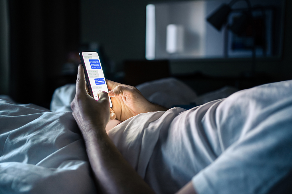Fotografia de um homem deitado mexendo no celular.