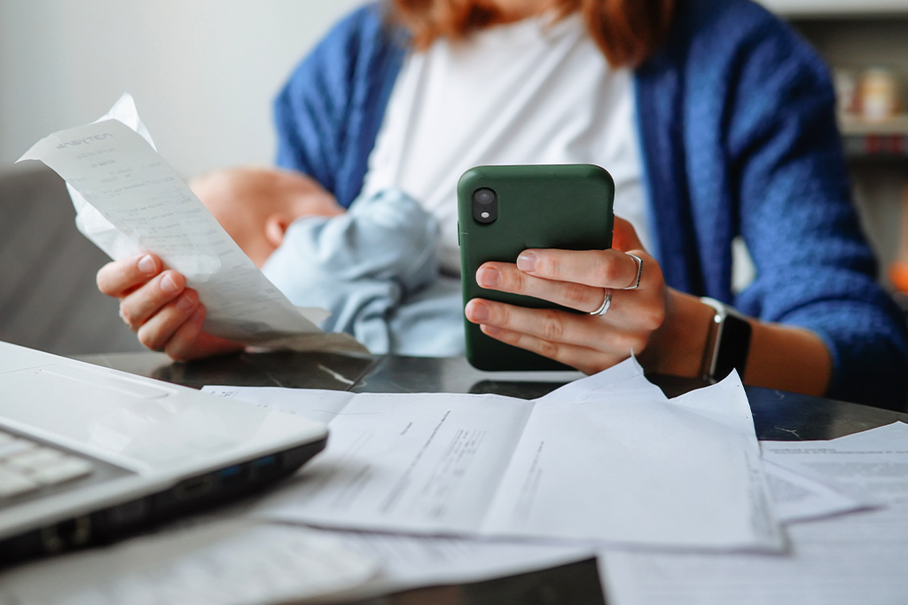 Uma mulher olhando boletos com um bebê no colo.