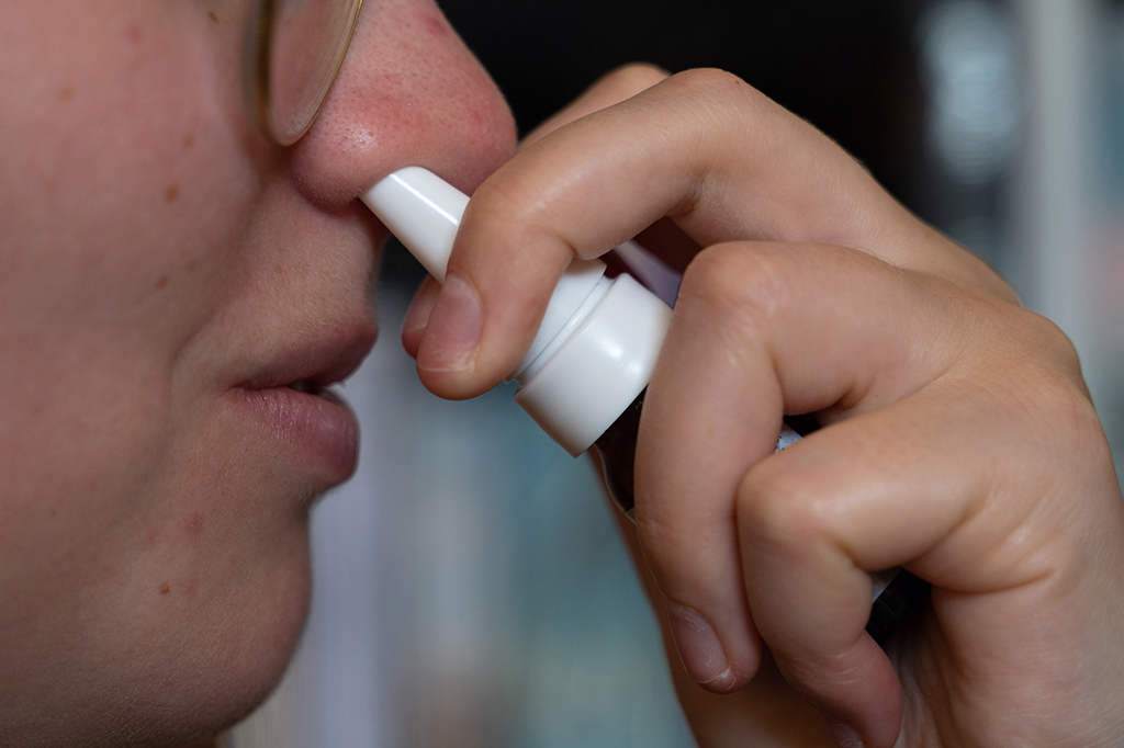 Fotografia de uma mulher usa spray nasal.