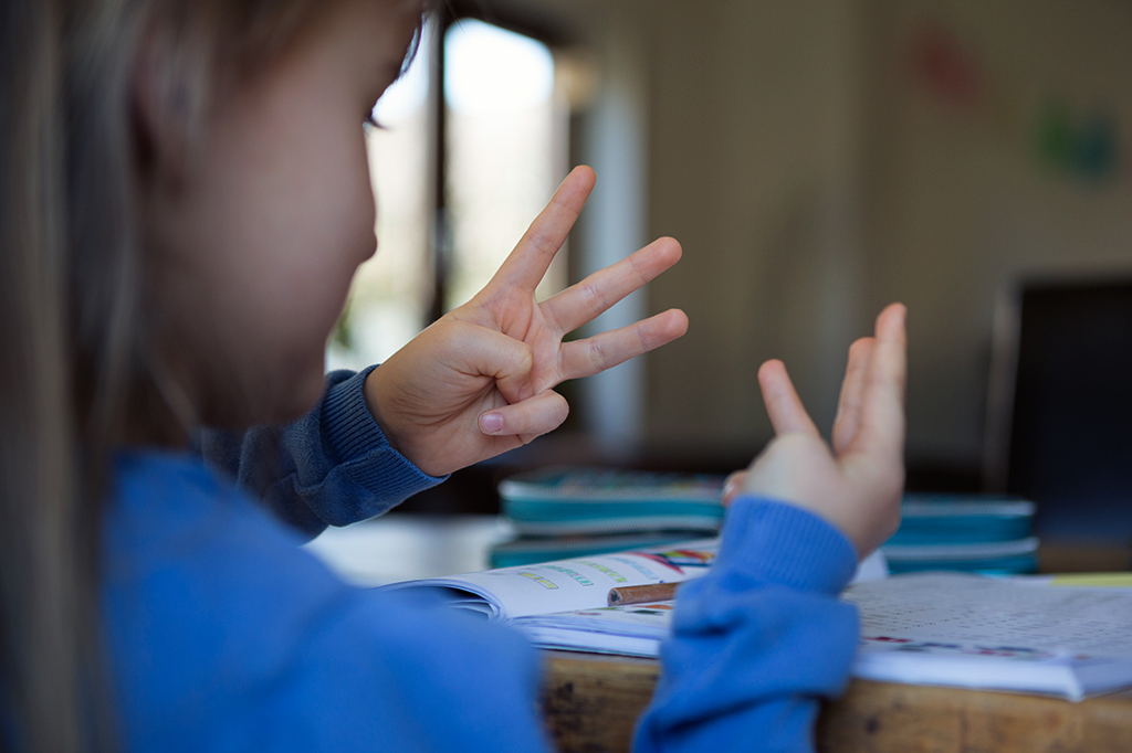 Fotografia de uma criança contando com os dedos enquanto faz a lição de casa de matemática.