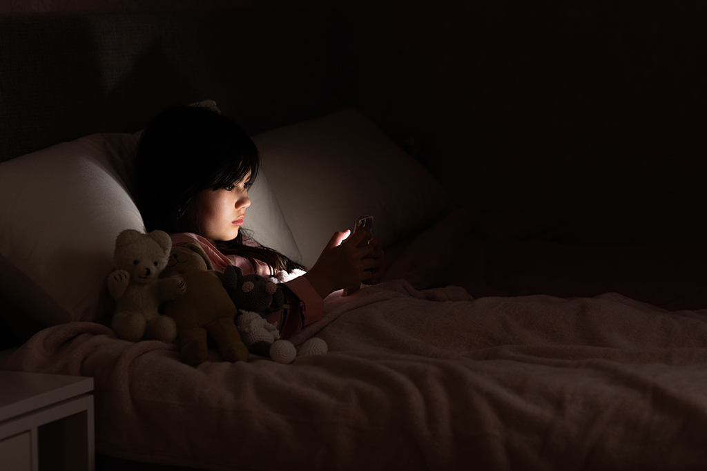 Fotografia de uma criança deitada mexendo no celular.