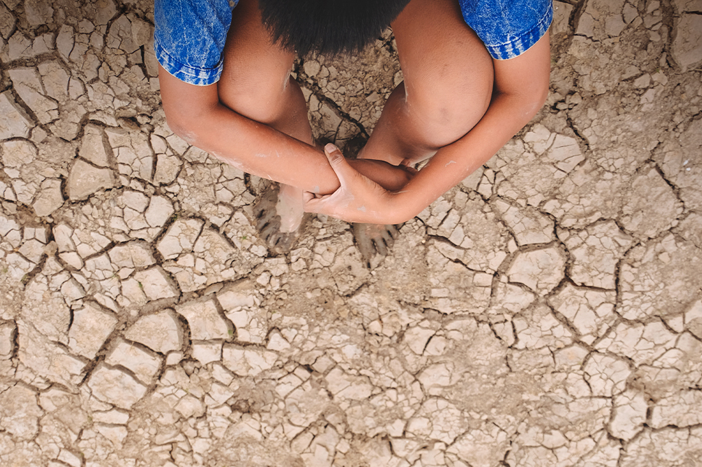 Fotografia da vista de alto ângulo de um menino sentado no campo rachado.