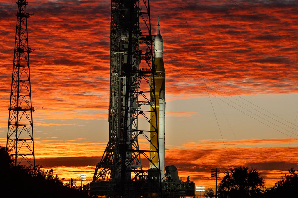Fotografia de Nuvens e o Sol iluminam o céu na quarta-feira, 28 de janeiro de 2026, enquanto o foguete Artemis II SLS (Space Launch System) da NASA e a espaçonave Orion permanecem na vertical no Complexo de Lançamento 39B do Centro Espacial Kennedy, na Flórida.