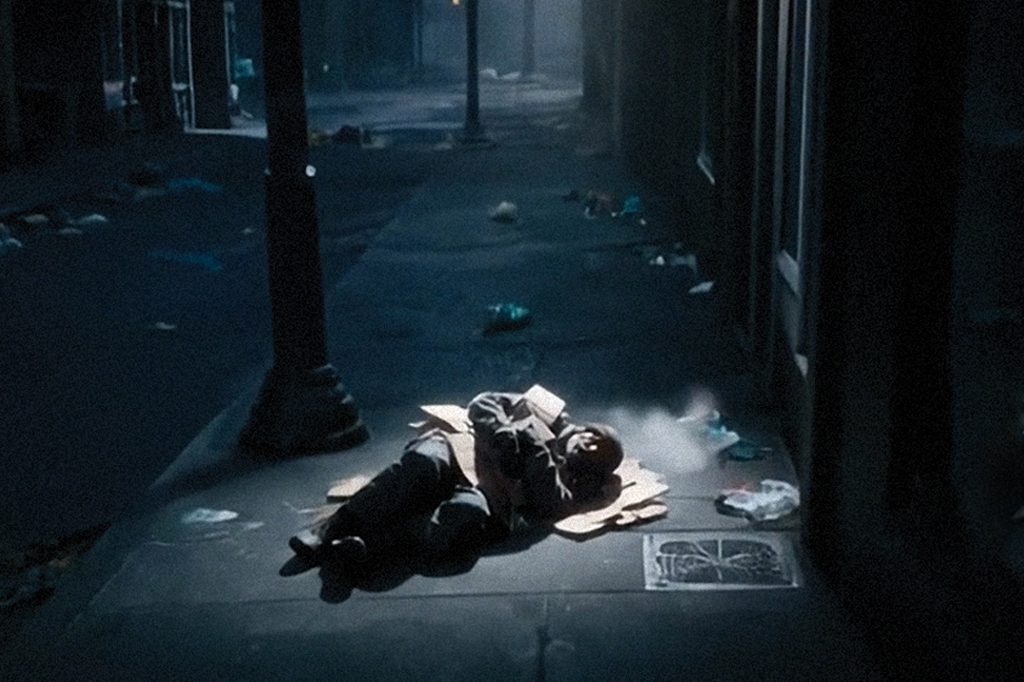 Imagem de um homem dormindo ao relento numa cidade suja e escura.