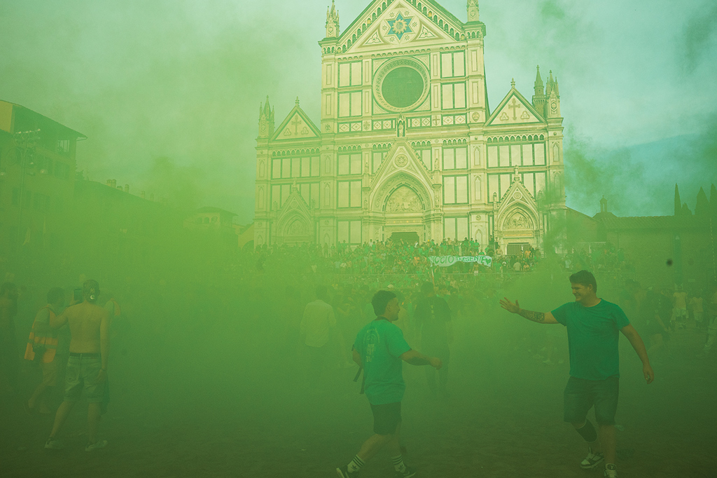 Fotografia de uma cena durante o torneio Calcio Storico Fiorentino de 2025: uma igreja ofuscada por uma nuvem de fumaça verde.