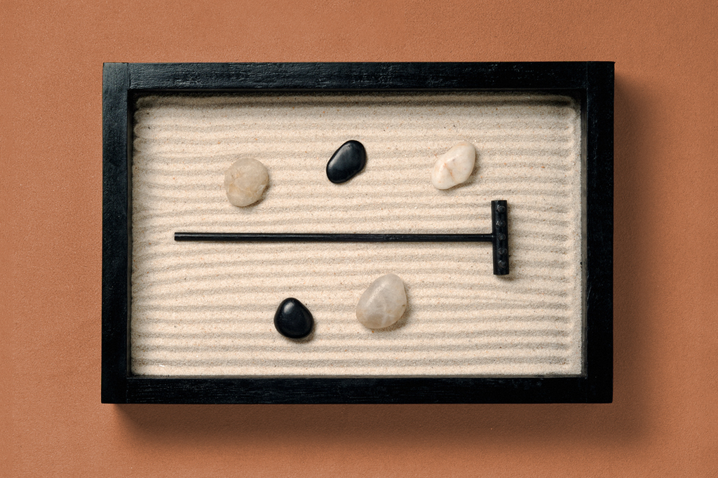 Imagem, em fundo marro, de um pequeno jardim zen de madeira contendo areia, pedras e um pequeno rastelo.