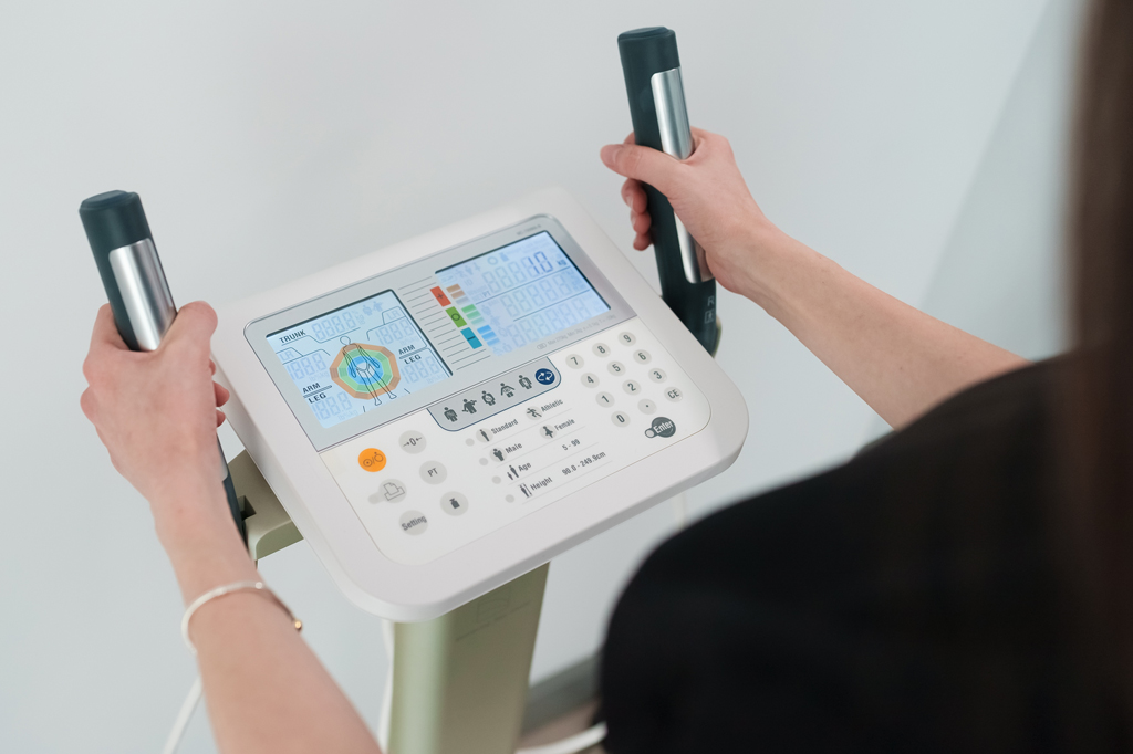 Imagem de uma mulher segurando sensores de uma balança de bioimpedância.